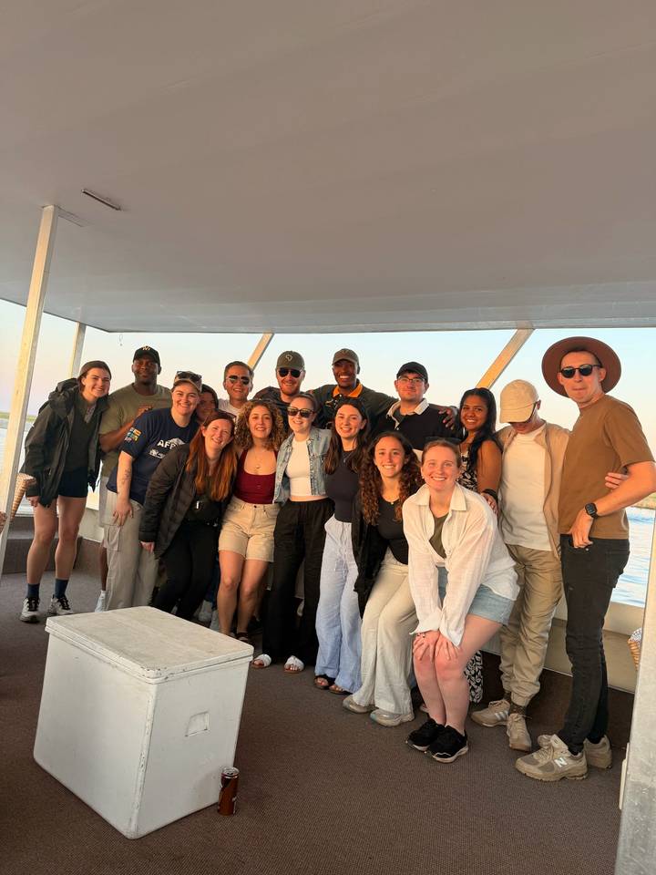Large group of smiling travellers posing together on a covered boat deck.