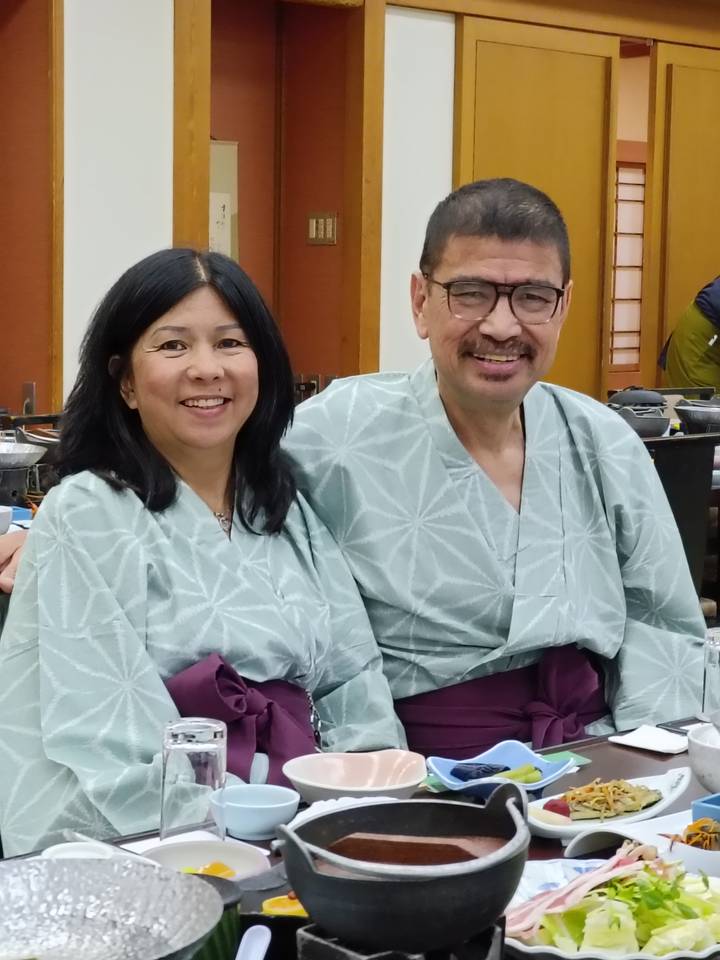 Smiling couple dressed in traditional yukata seated inside a Japanese ryokan dining hall.