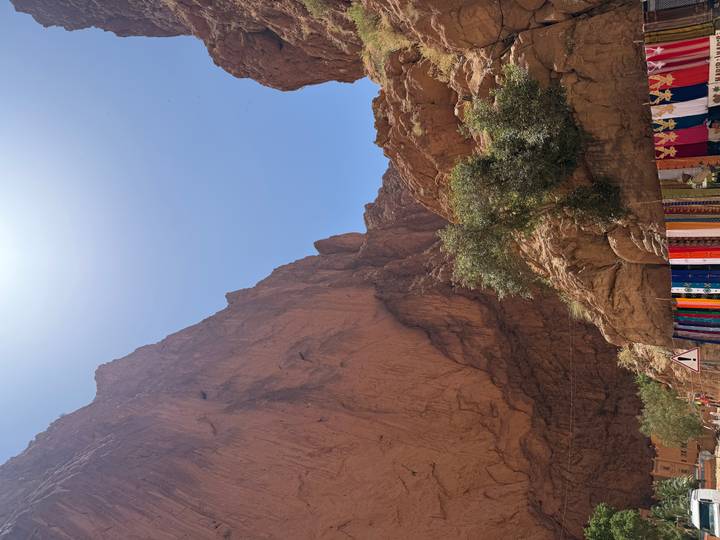 Steep red-rock walls of Todra Gorge rising toward a bright midday sun with colourful market stalls below