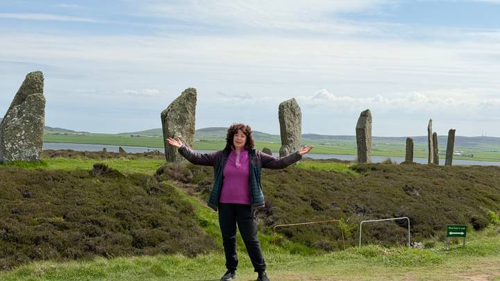 Traveler spreading arms happily in front of a row of Neolithic standing stones beside the sea