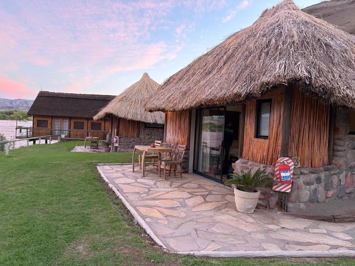 Thatched-roof riverside chalets with stone patios and lawn at dusk