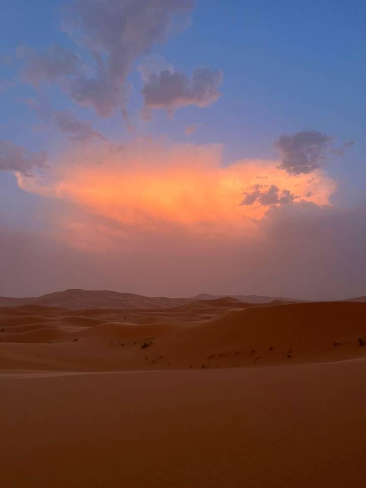 Soft pink and orange clouds light up the sky over rolling sand dunes at dusk