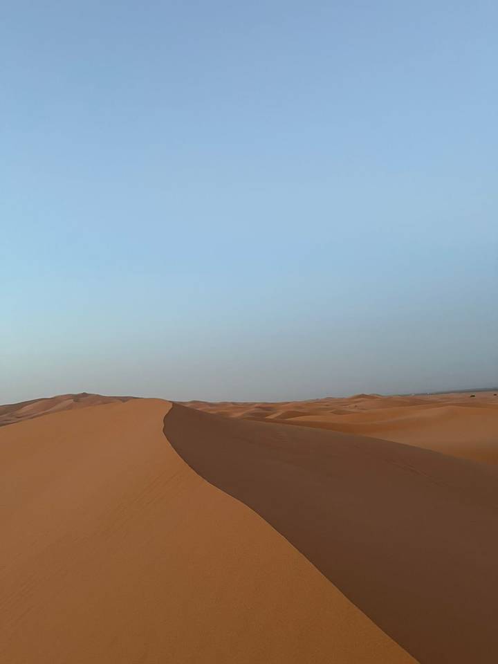 Minimalist view of a curving sand ridge against a pale blue sky in the desert