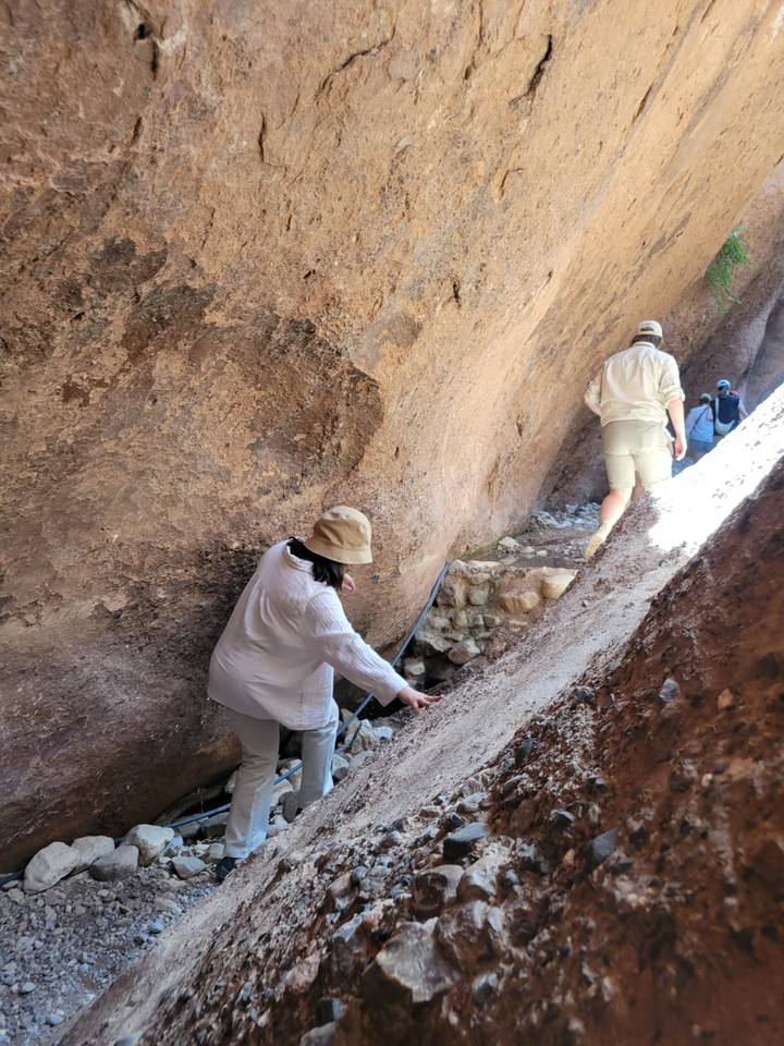 Travellers squeeze through a rocky ravine using hands for balance on a narrow path