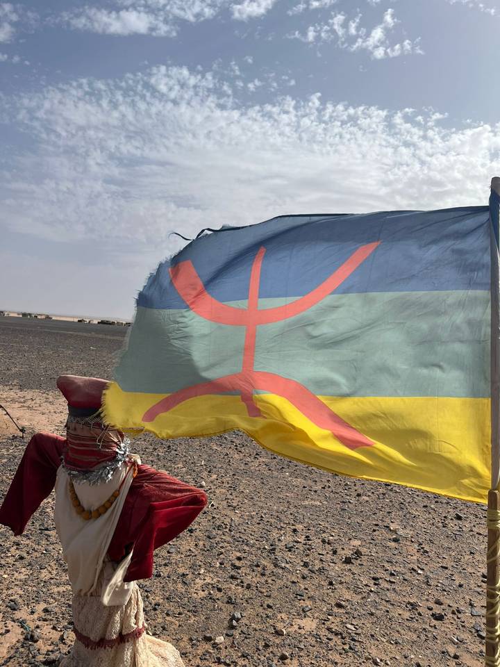 Amazigh (Berber) flag ripples in the desert wind with black gravel plain behind