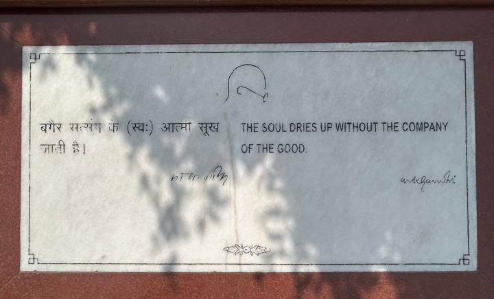 Marble plaque engraved with a Gandhi quote in English and Hindi, partially shaded by leaves.