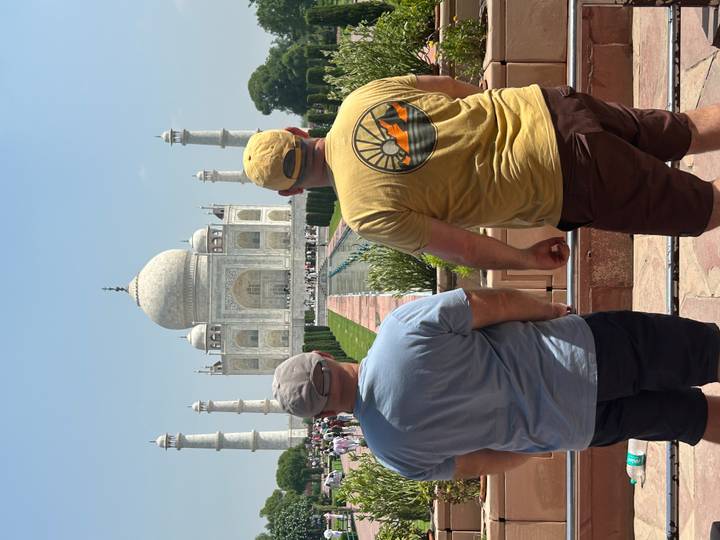 Two men from behind admire the central vista leading to the Taj Mahal on a sunny day.