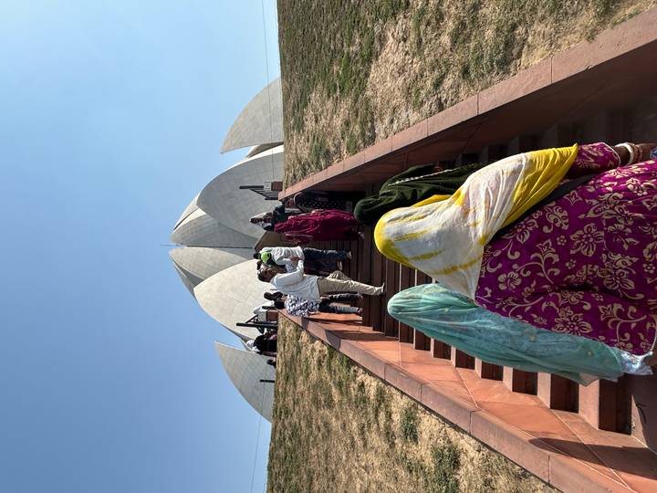 Visitors climb the stairs toward Delhi’s Lotus Temple under a cloudless blue sky.