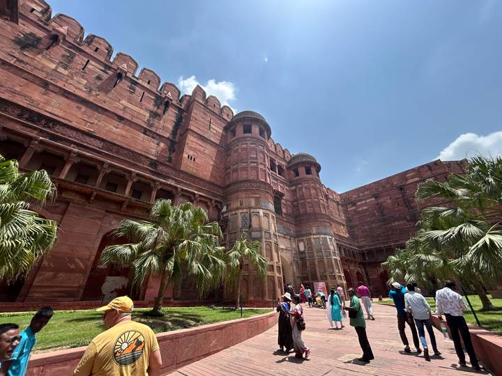 Towering red sandstone walls and bastions of Agra Fort loom over palm trees and tourists below.