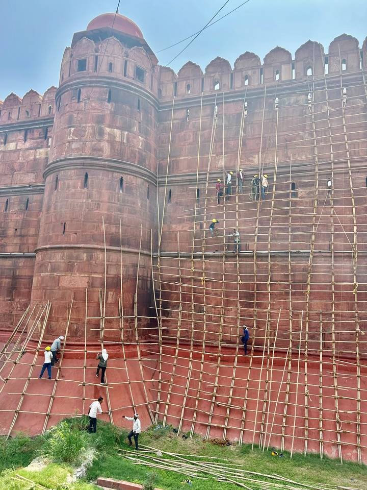 Construction workers scaling bamboo scaffolding on a massive red fort wall during restoration.