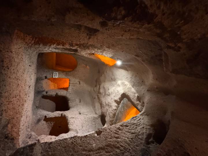 Dimly lit chambers carved from volcanic rock form a maze-like underground city illuminated by soft orange lighting.