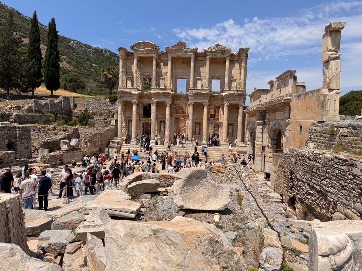 Crowds explore the ornate façade of the ancient Library of Celsus amid scattered marble ruins.