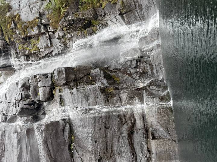 Close view of cascading fjord waterfalls hitting rock faces above dark water
