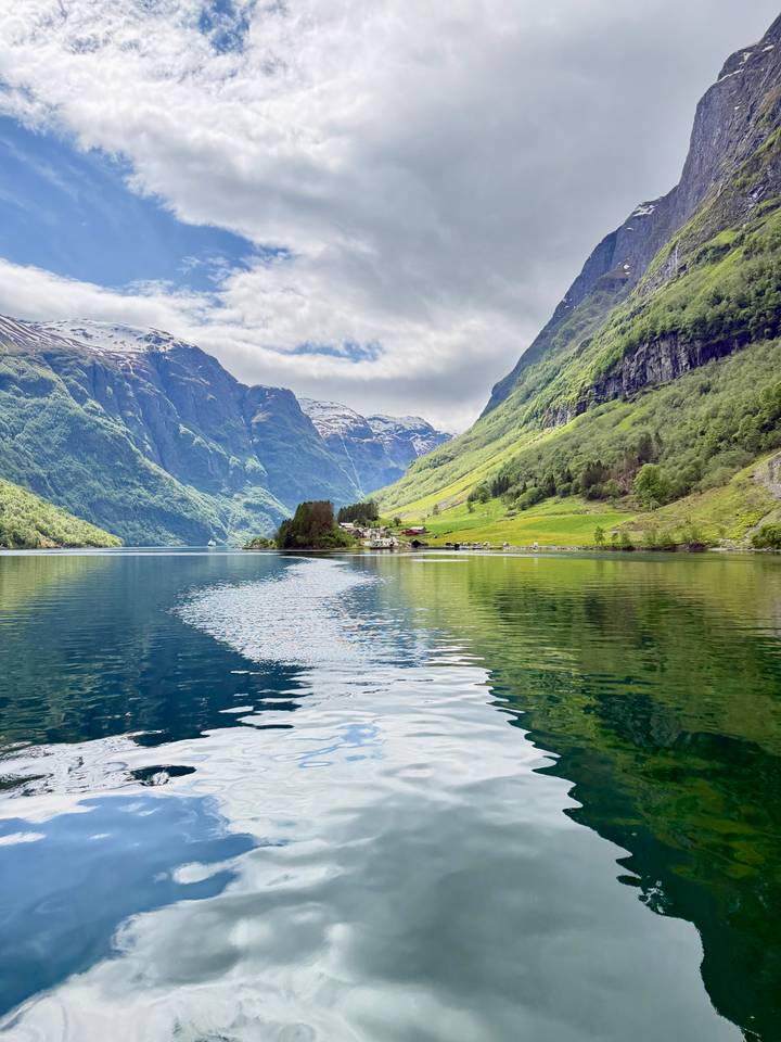 Mirror-calm fjord reflects emerald slopes and a tiny village nestled beneath towering peaks