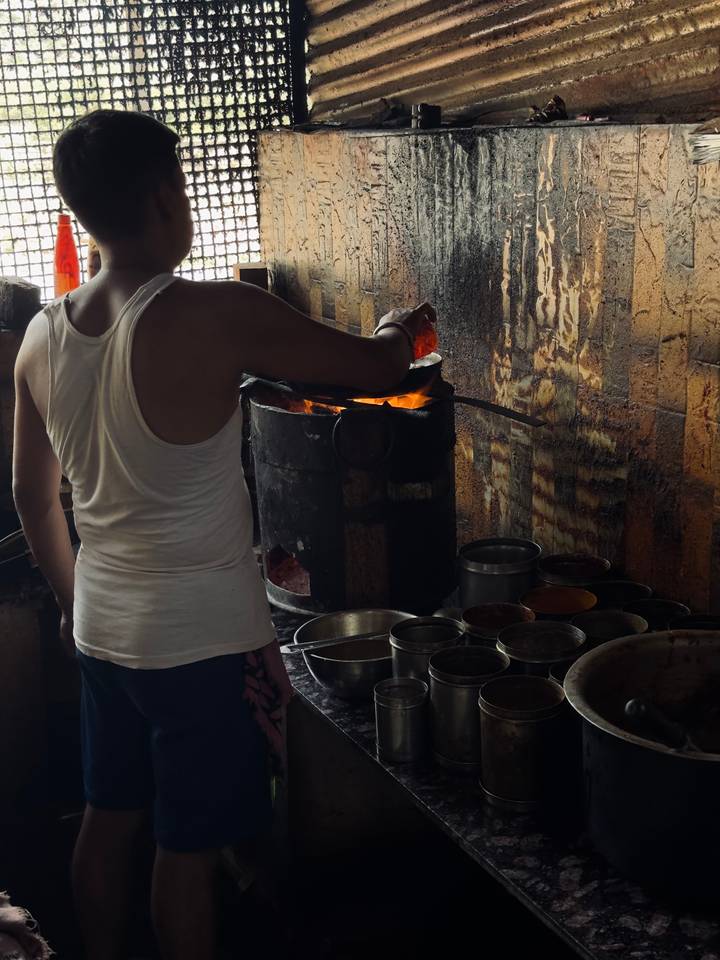 Street vendor stirs a glowing charcoal stove surrounded by metal spice tins