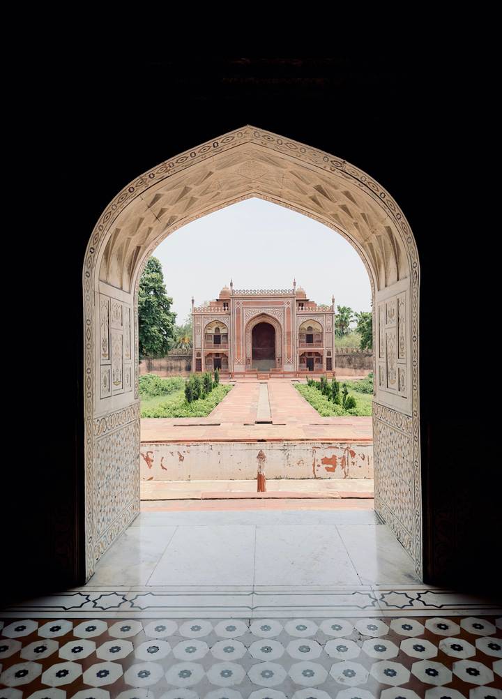Symmetrical Mughal tomb framed by ornate marble archway with lush gardens ahead