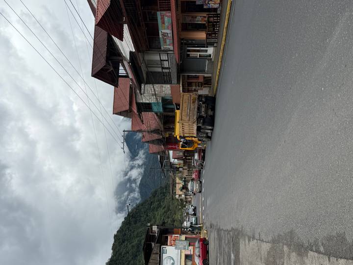 A mountain town main road under cloudy skies with timber-roofed buildings and vehicles parked along the asphalt.