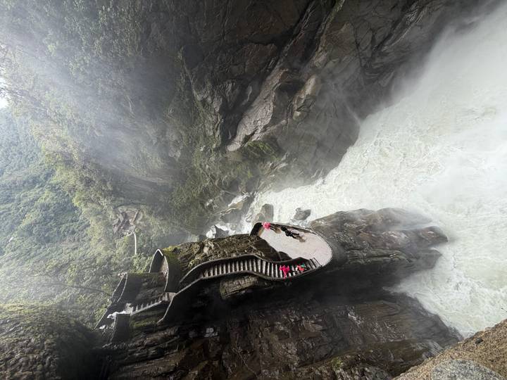 Visitors descend curved stone stairs beside the dramatic Pailon del Diablo gorge where a powerful river surges below misty cliffs.