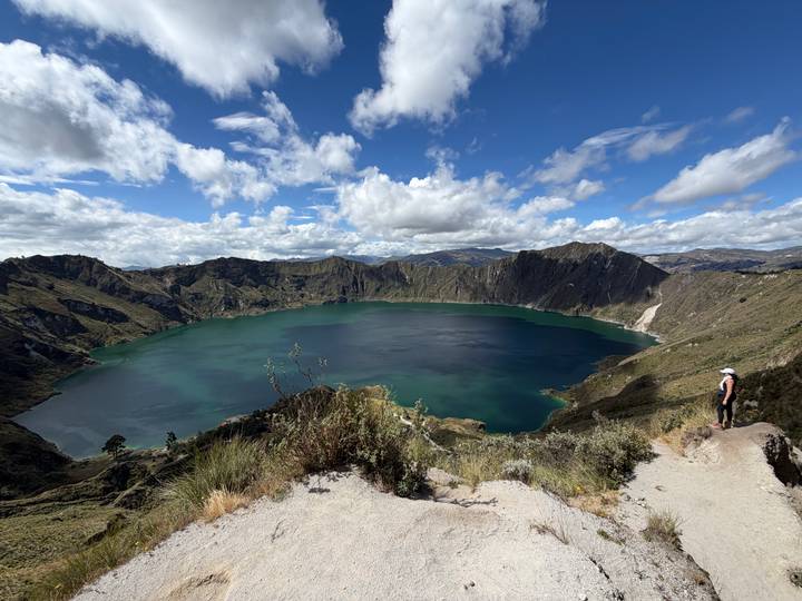 A panoramic view of Quilotoa’s turquoise crater lake surrounded by steep volcanic cliffs under a partly cloudy sky.