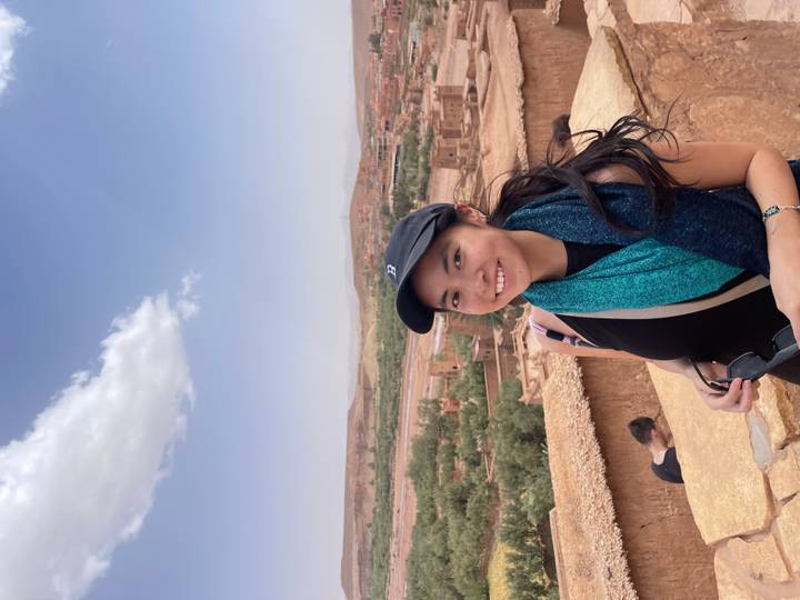 A smiling traveler poses on a viewpoint overlooking the ancient adobe kasbahs and arid plains of Ait Benhaddou.