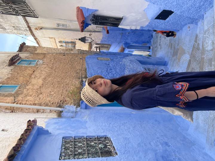 A woman in a straw hat stands along a narrow blue alleyway of Chefchaouen’s medina.