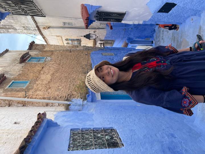 Smiling traveler in embroidered dress poses in Chefchaouen’s iconic blue street.