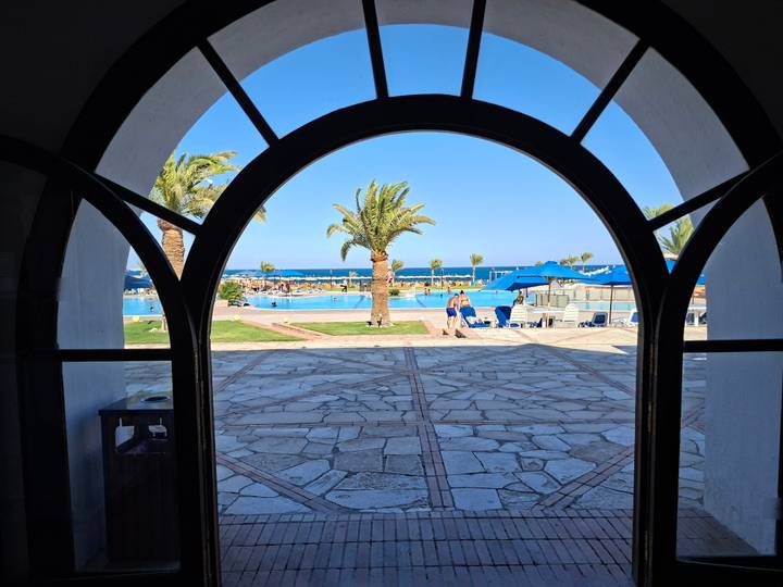Resort view framed by an arched doorway showing pool, palms and the Red Sea.