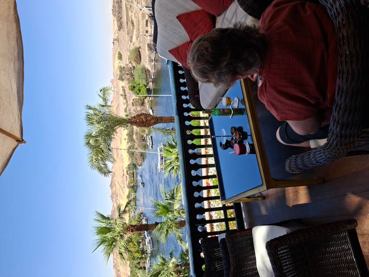 Woman relaxing on a shaded terrace overlooking the Nile River and palm-lined banks.