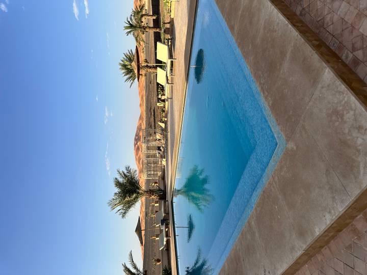 Serene swimming pool at desert lodge overlooking rolling sand dunes at sunset.