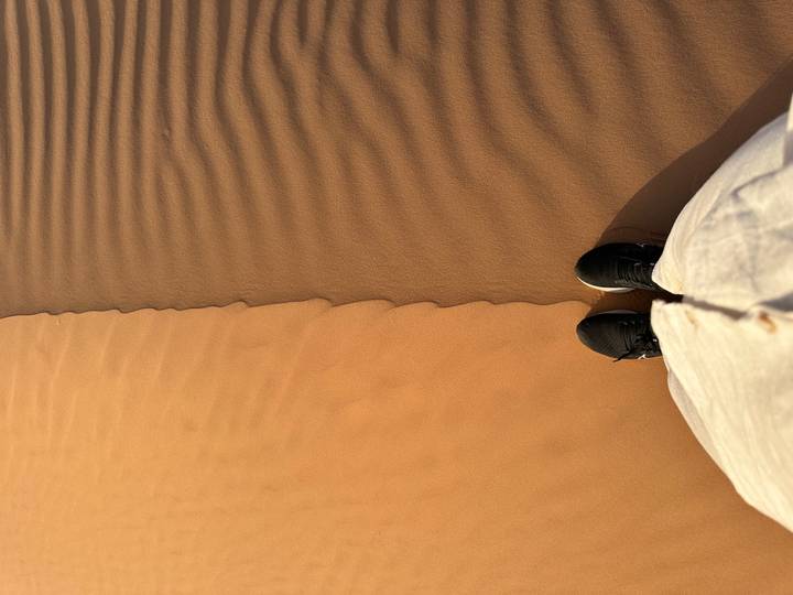 Point-of-view shot of traveler’s shoes standing where two colors of dune sand meet.