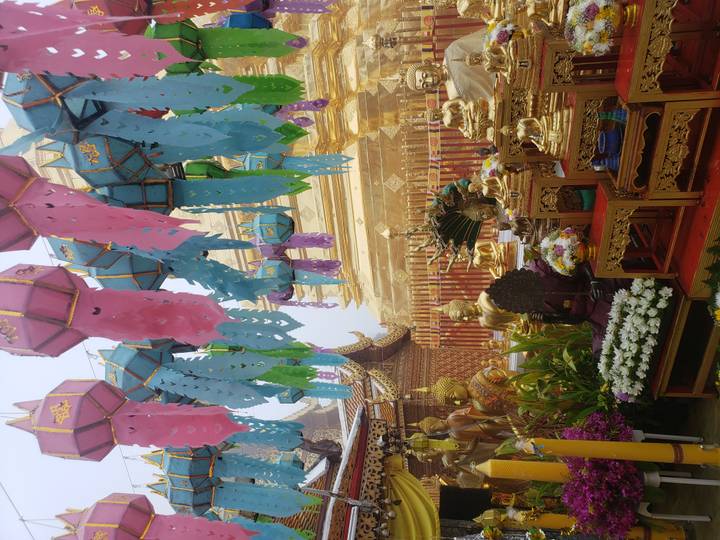 Colorful lanterns hang before a gleaming golden stupa and ornate statues in a fog-kissed temple courtyard.