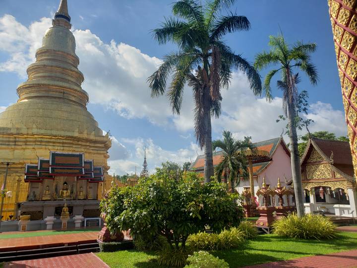 Golden temple stupa and palm trees rise above lush greenery beneath a bright tropical sky.