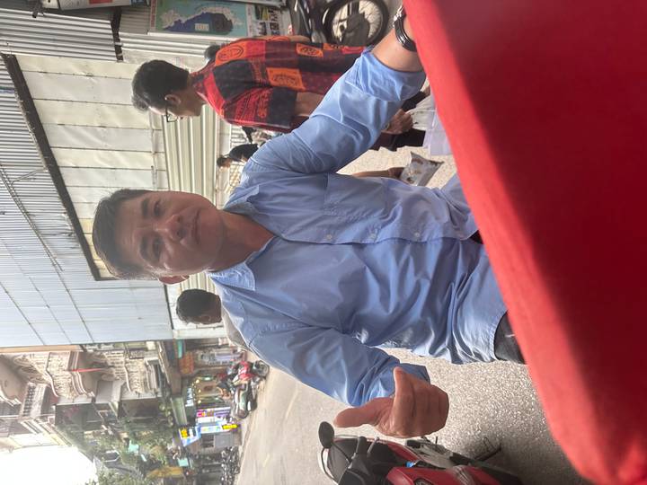 Man in a blue shirt gives a thumbs-up while riding through a busy city street.
