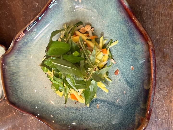 Plate with a fresh shredded mango salad garnished with herbs and peanuts.