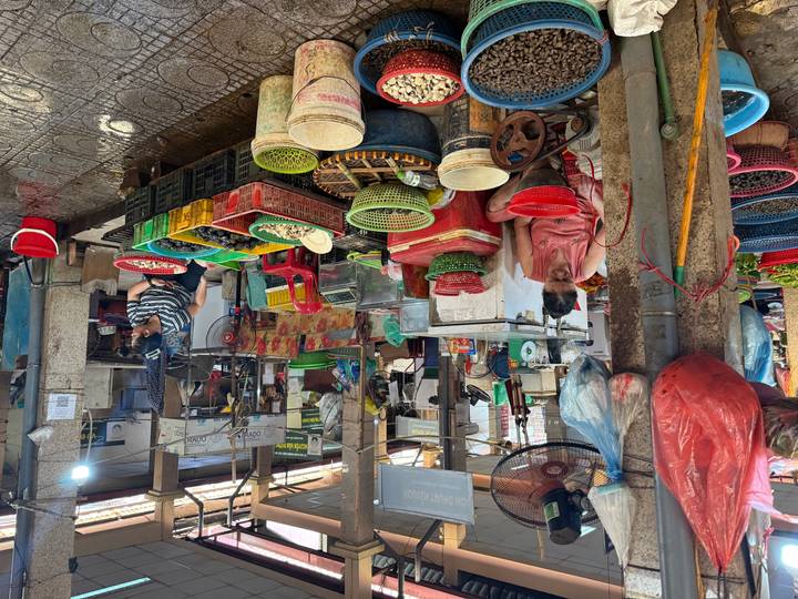 Bustling indoor market with vendors sorting produce, colorful baskets, and wet tile floors.
