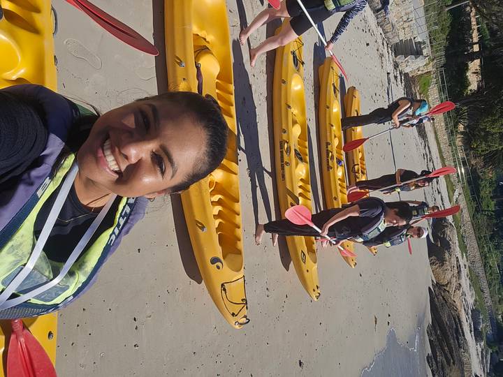Kayak group poses with yellow sea kayaks lined up on sandy beach, selfie in foreground.