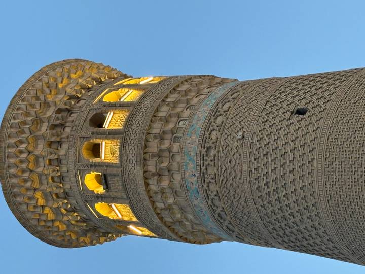 Illuminated brick minaret of Bukhara with ornate geometric patterns against twilight sky.