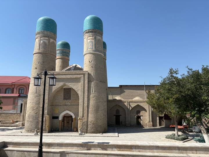 Historic Chor Minor mosque with four turquoise domes and brick facade under a bright blue sky.