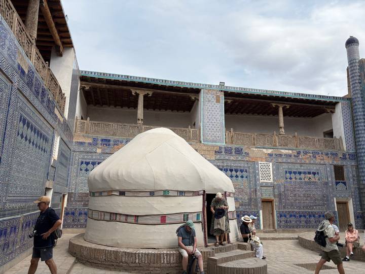 Courtyard lined with vivid blue mosaic tiles featuring a traditional yurt and tourists exploring.