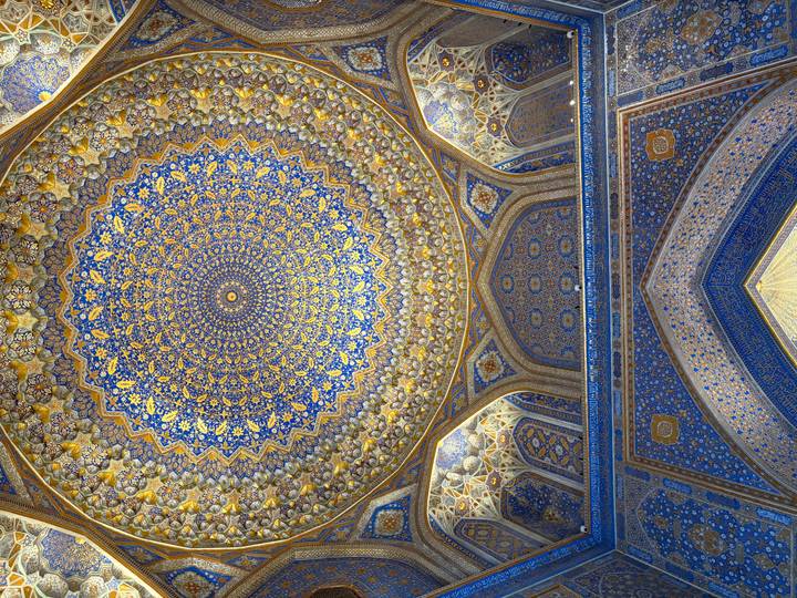 Intricately patterned blue-and-gold Islamic dome ceiling inside a historic madrasah.