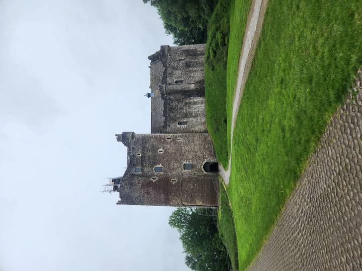 Stone medieval Doune Castle rising above a grassy embankment on a cloudy day.