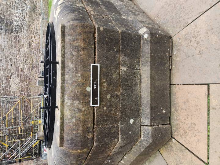 Close-up of an old stone well with a small label sign inside a castle yard.