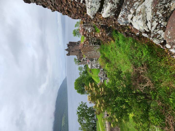 Ruins of Urquhart Castle overlooking Loch Ness surrounded by lush greenery.