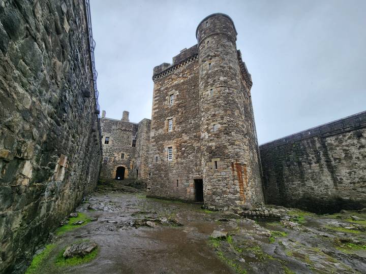 Stone tower and walls inside a medieval castle courtyard with wet cobblestones.