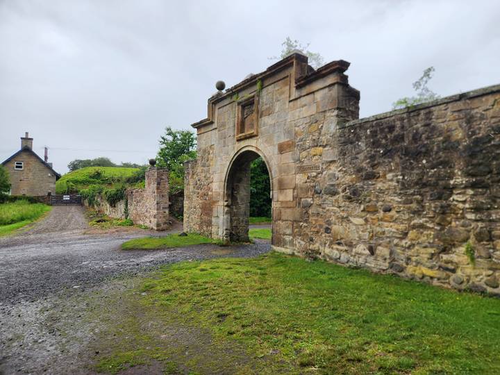 Old stone arch gate leading to a country estate surrounded by greenery.