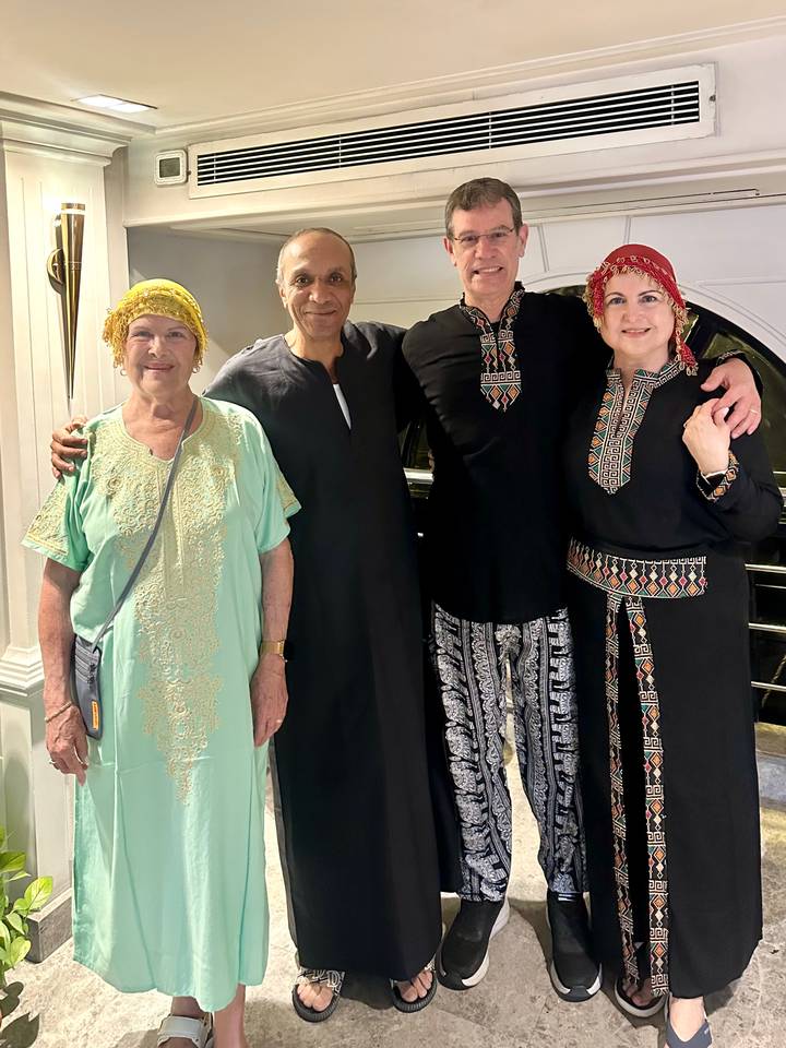 Four travellers dressed in traditional Egyptian galabeyas smile for an indoor photo.