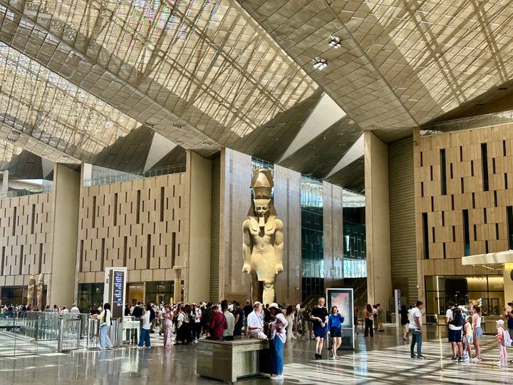 Grand entrance hall of the new Egyptian museum with towering statue of Ramses II and crowds of visitors.