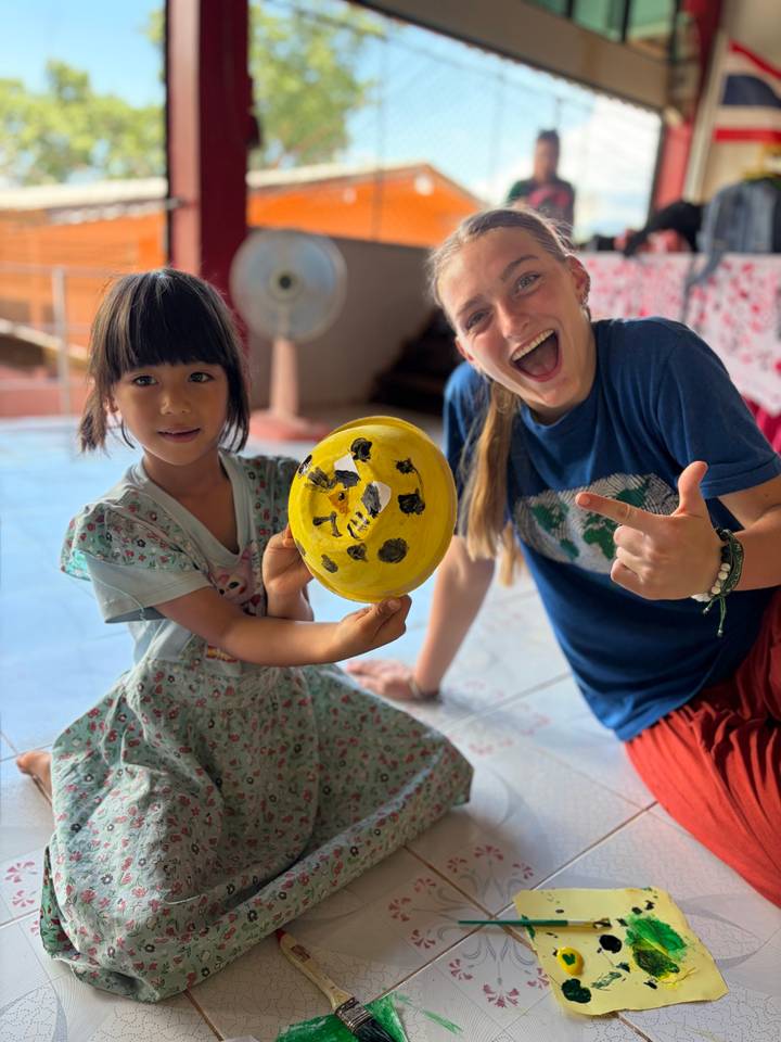 Volunteer and young child proudly display a painted craft plate indoors.
