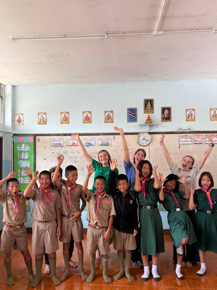 Volunteers and schoolchildren cheer in a colorful classroom decorated with Thai icons.