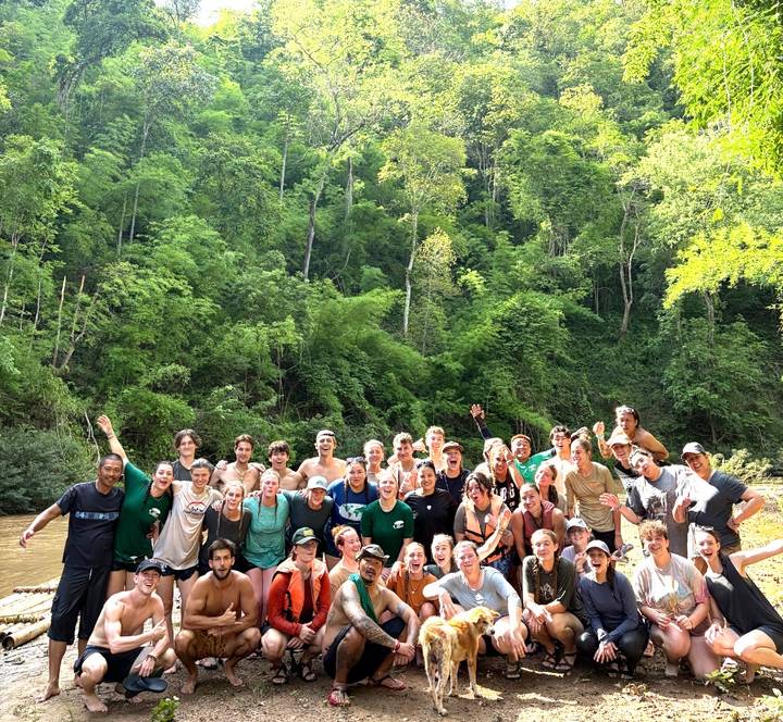 Energetic group stands knee-deep in a forest river celebrating after a trek.